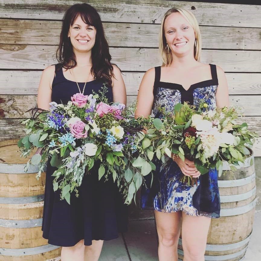 Valerie and Kayla holding large bouquets of flowers filled with roses, violet flowers, and greenery