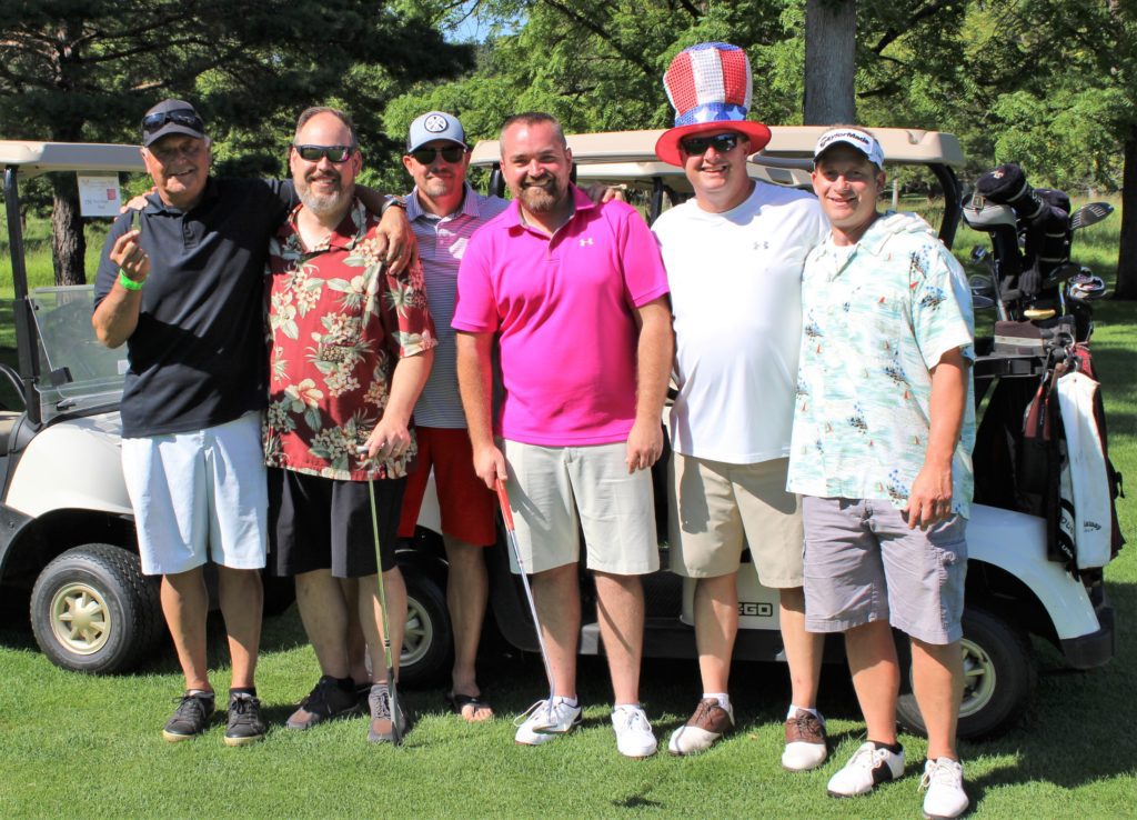 Six golfers pose for a photo at the Hometown Golf Challenge near their golf carts on the golf course
